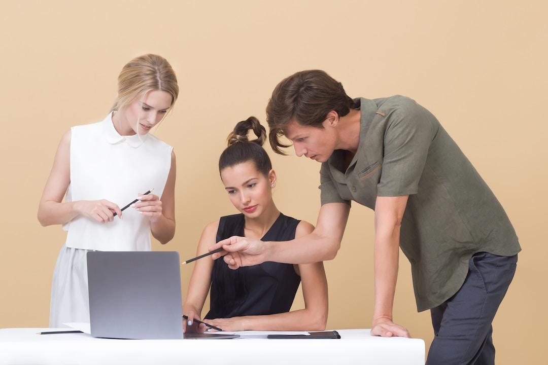 Three people looking at a laptop screen against a tan background discuss professional services automation's benefits.
